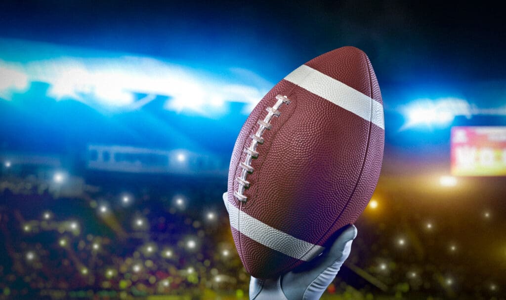 Hand holding a football in front of a professional football stadium