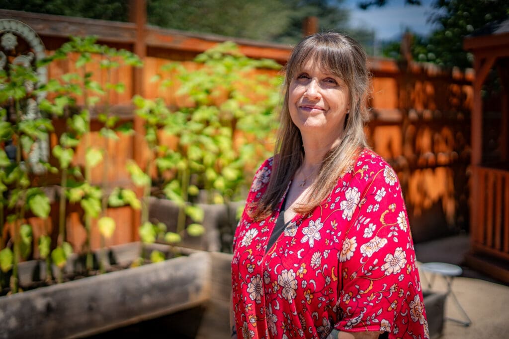 Jennifer stands in front of a fence and garden beds.